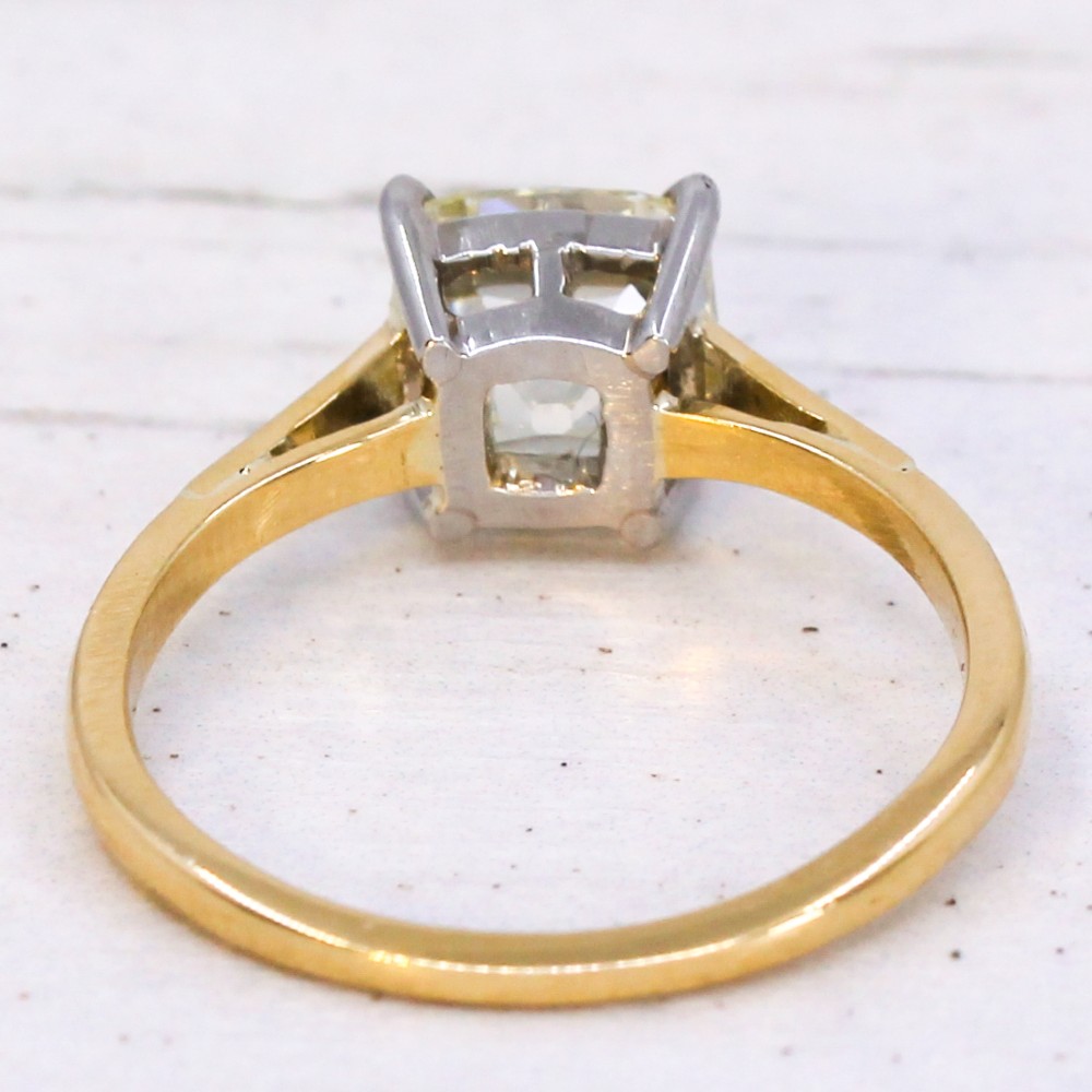 A vintage solitaire engagement ring featuring an old cut cushion diamond held in platinum claws on a tapered yellow gold band. View V