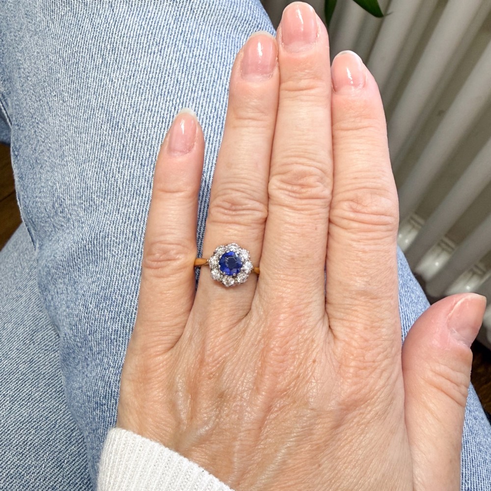 A yellow gold vintage ring featuring a central round blue sapphire encircled by a halo of brilliant-cut diamonds. View VI