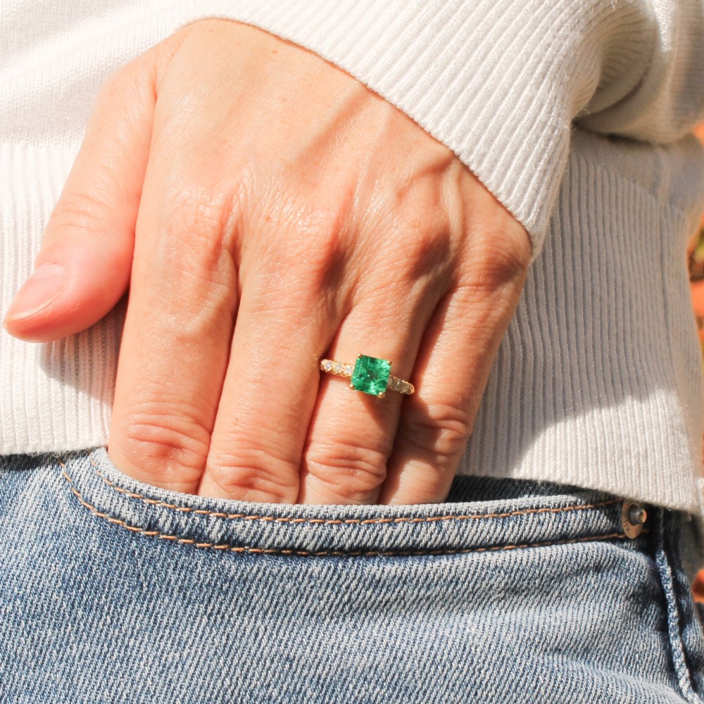 A yellow gold ring featuring a central square-cut green emerald held in a four-prong setting, accented by three small round diamonds on each shoulder. View II