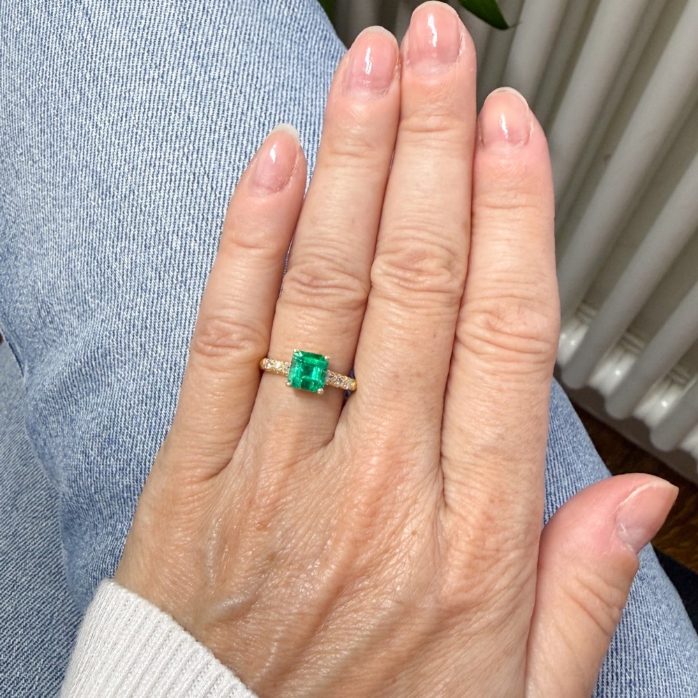 A yellow gold ring featuring a central square-cut green emerald held in a four-prong setting, accented by three small round diamonds on each shoulder. View VII