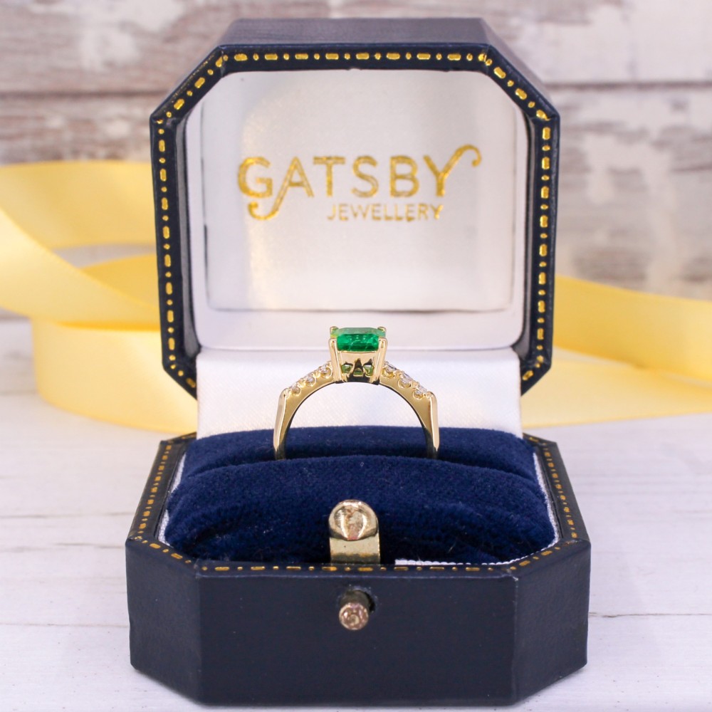 A yellow gold ring featuring a central square-cut green emerald held in a four-prong setting, accented by three small round diamonds on each shoulder. View IX