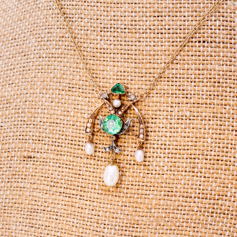 An Art Nouveau openwork gold pendant featuring a central round green emerald, diamond accents, and hanging natural pearl drops.