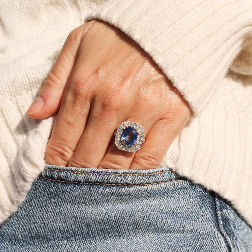 An antique Edwardian cluster ring featuring a central cushion-cut blue Ceylon sapphire surrounded by a halo of diamonds set in platinum and yellow gold. View VI