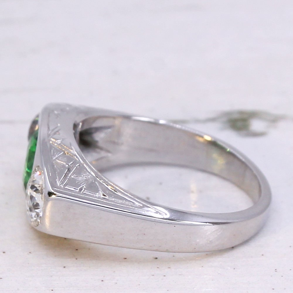 A white metal ring featuring a central round green tsavorite garnet flanked by two old cut diamonds set within a carved band. View IV