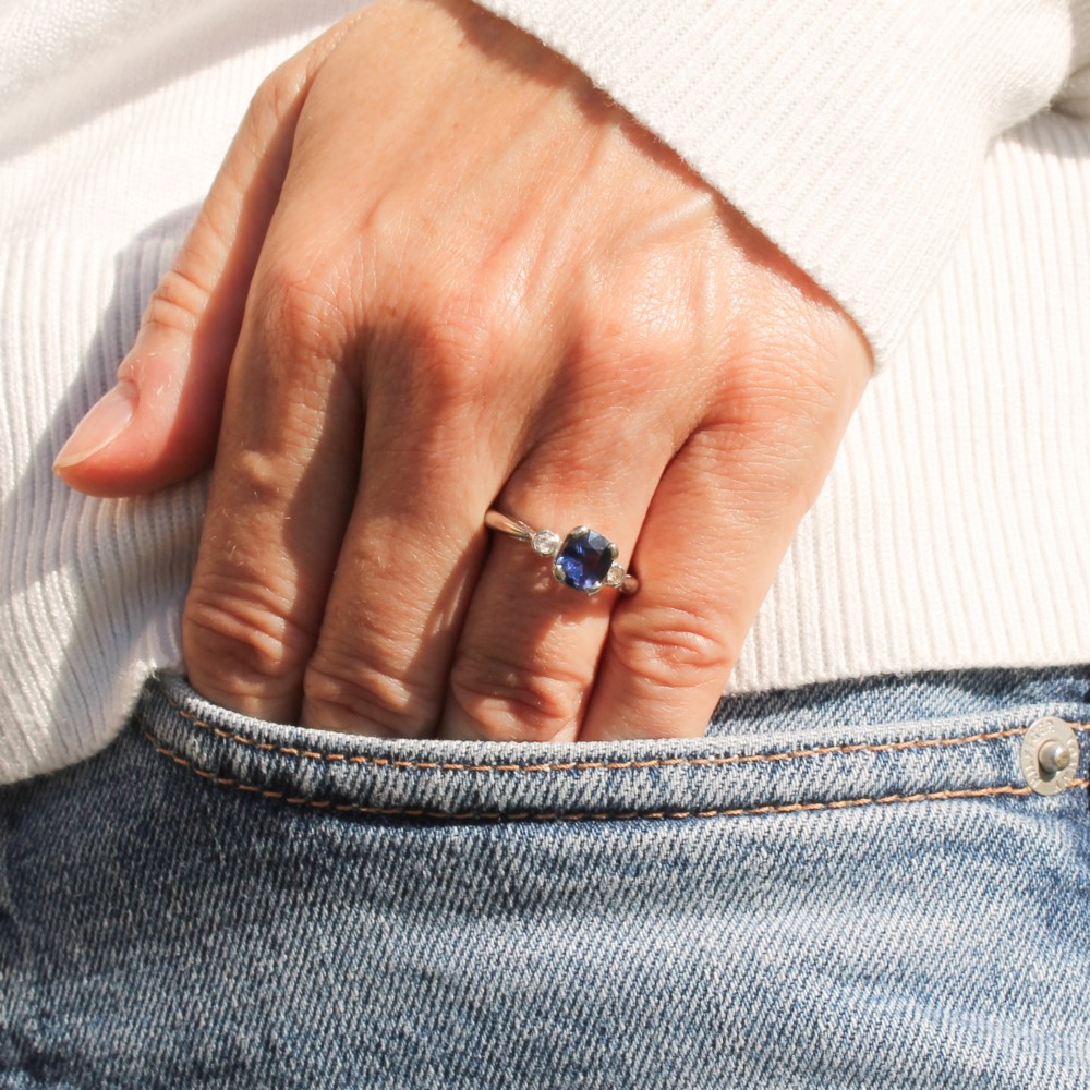 A platinum ring featuring a central cushion-cut blue sapphire held in a claw setting, flanked by a small round diamond on each shoulder. View II