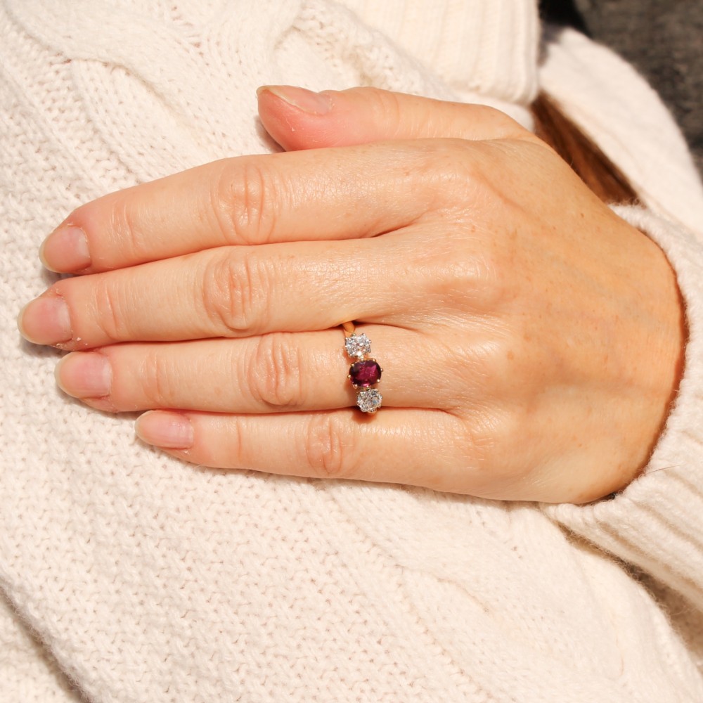 An antique yellow gold trilogy ring featuring a central cushion-cut red ruby flanked by two old-cut diamonds in claw settings. View II