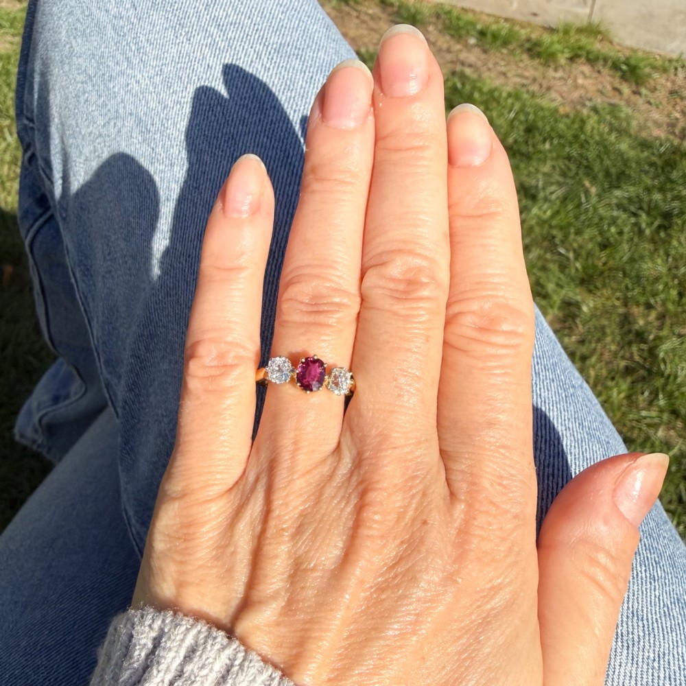 An antique yellow gold trilogy ring featuring a central cushion-cut red ruby flanked by two old-cut diamonds in claw settings. View VII