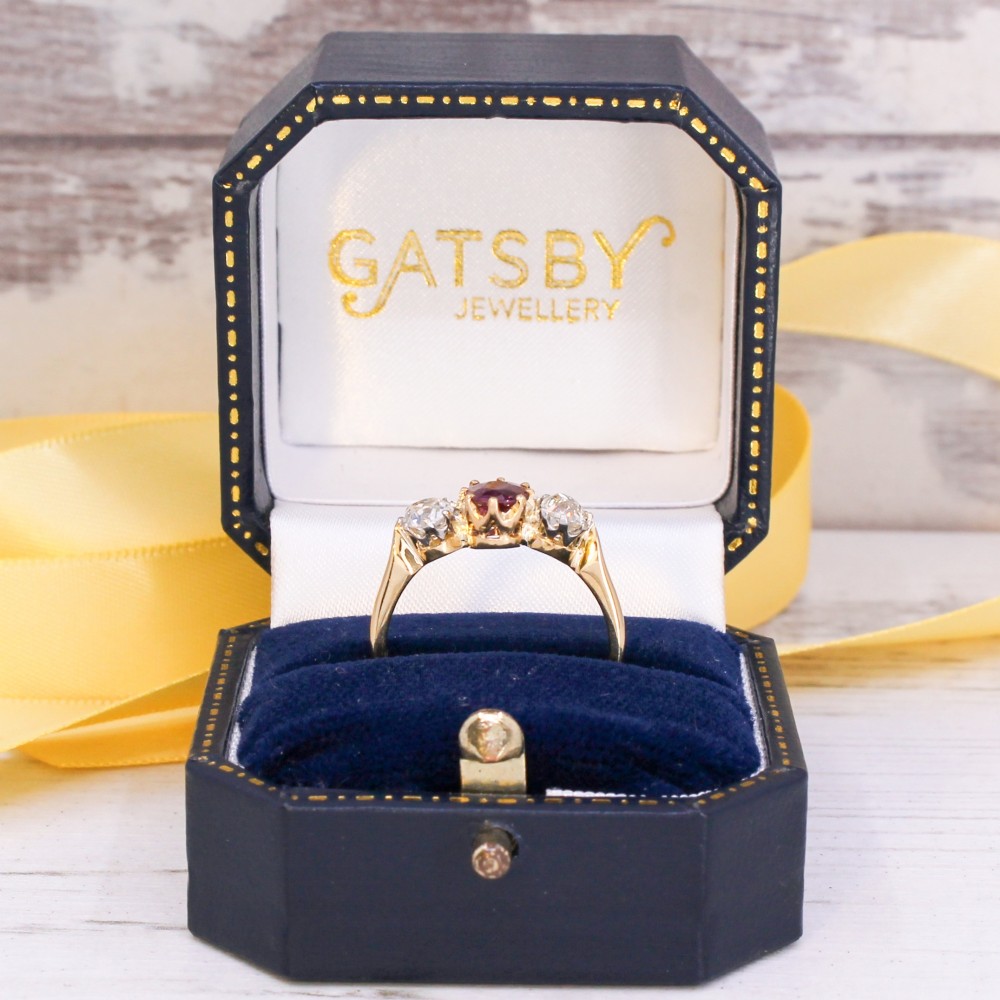 An antique yellow gold trilogy ring featuring a central cushion-cut red ruby flanked by two old-cut diamonds in claw settings. View IX