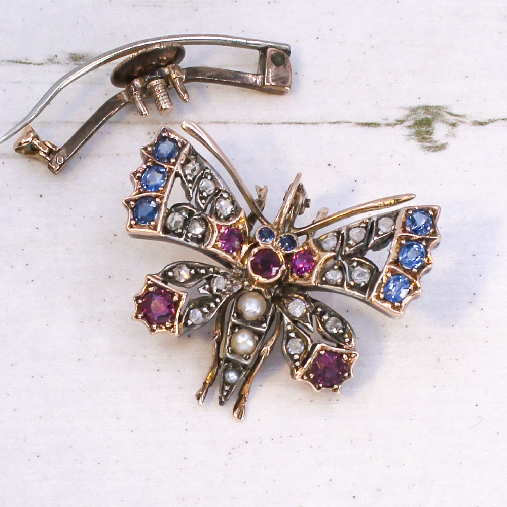 A Victorian butterfly brooch set with rubies, sapphires, diamonds, and natural pearls in silver and gold. View V