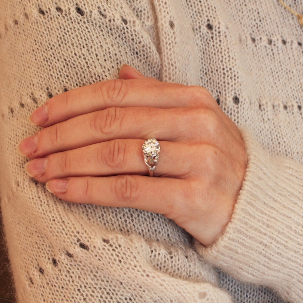 A vintage mid-century platinum engagement ring featuring a central round brilliant cut diamond flanked by baguette and round accent stones. View II