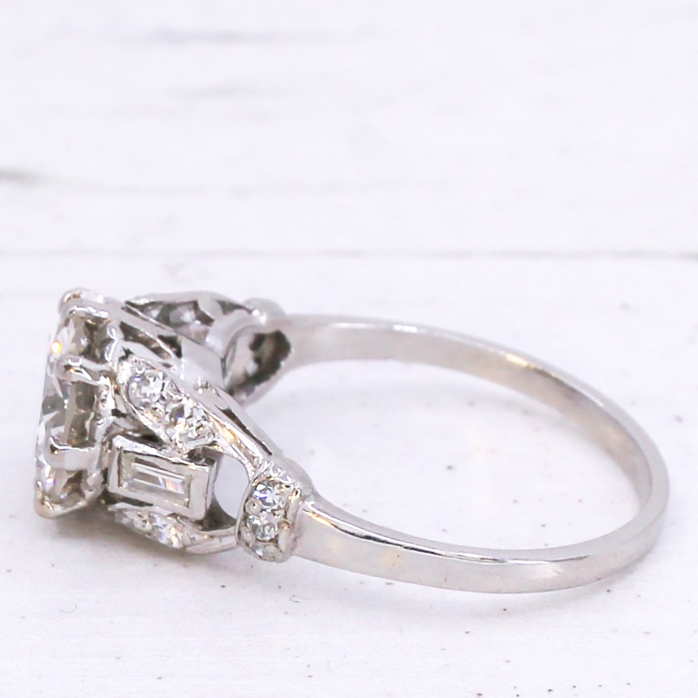 A vintage mid-century platinum engagement ring featuring a central round brilliant cut diamond flanked by baguette and round accent stones. View IV