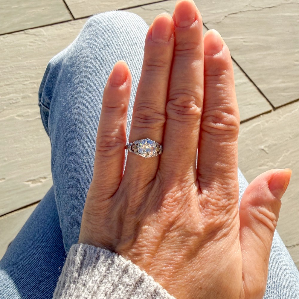 A vintage mid-century platinum engagement ring featuring a central round brilliant cut diamond flanked by baguette and round accent stones. View VI
