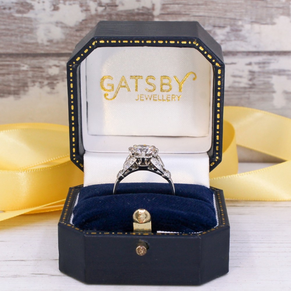 A vintage mid-century platinum engagement ring featuring a central round brilliant cut diamond flanked by baguette and round accent stones. View IX