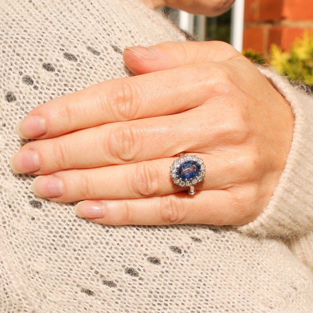 An oval blue Ceylon sapphire encircled by a halo of brilliant diamonds set on a silver metal band. View II