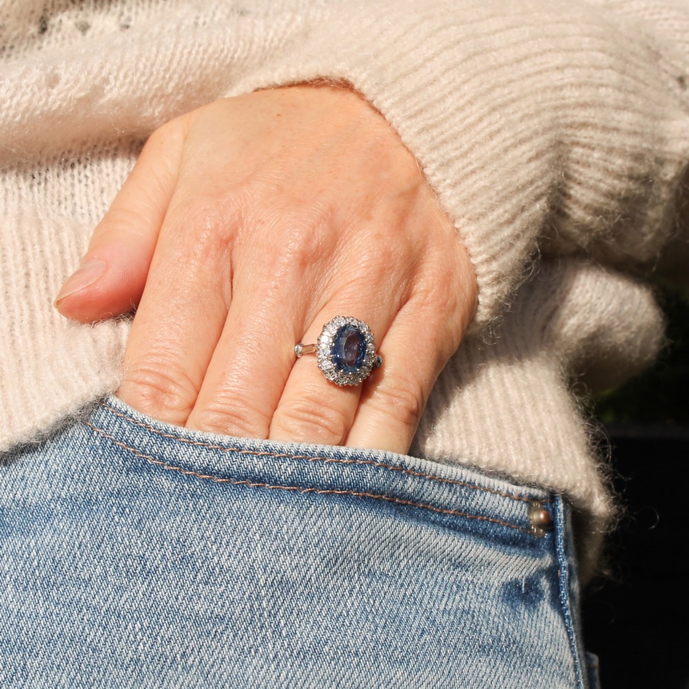 An oval blue Ceylon sapphire encircled by a halo of brilliant diamonds set on a silver metal band. View IX