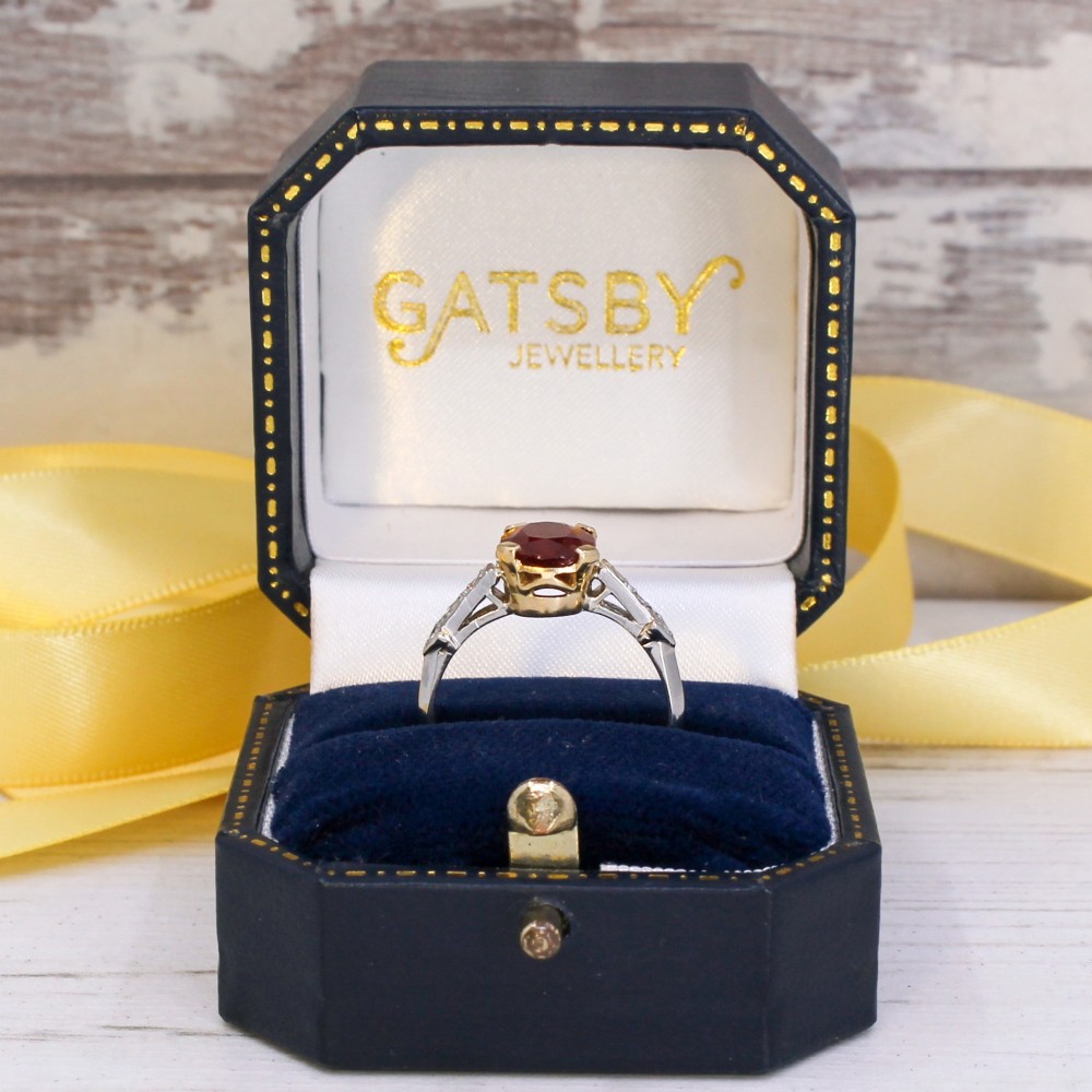 A vintage Art Deco solitaire ring featuring an oval red ruby in a gold setting on a silver-toned metal band with diamond-set shoulders. View IX