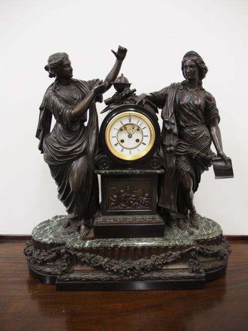 fig 1. A three-piece French antique clock garniture featuring a central mantel clock flanked by classical female figures and two standalone bronze male sculptures on dark marble bases.