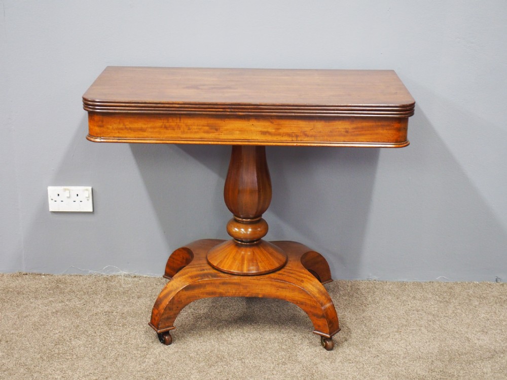 A 19th-century William IV mahogany fold-over table featuring a rounded rectangular top, a thick turned central pedestal, a concave quadform base, and brass castors. View II