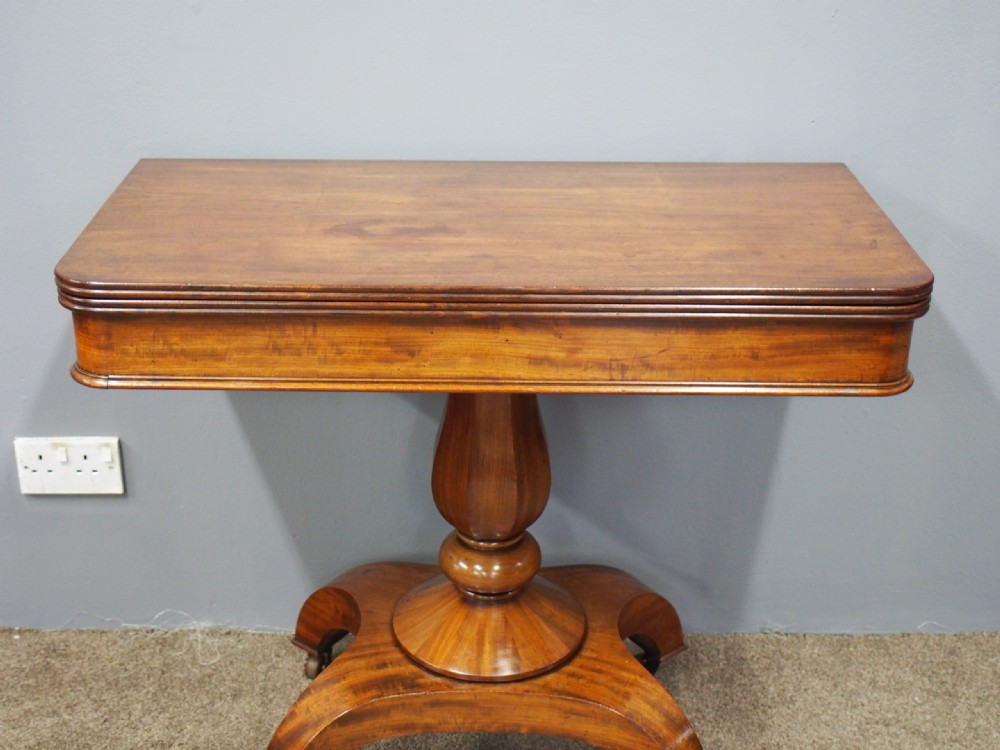 A 19th-century William IV mahogany fold-over table featuring a rounded rectangular top, a thick turned central pedestal, a concave quadform base, and brass castors. View III