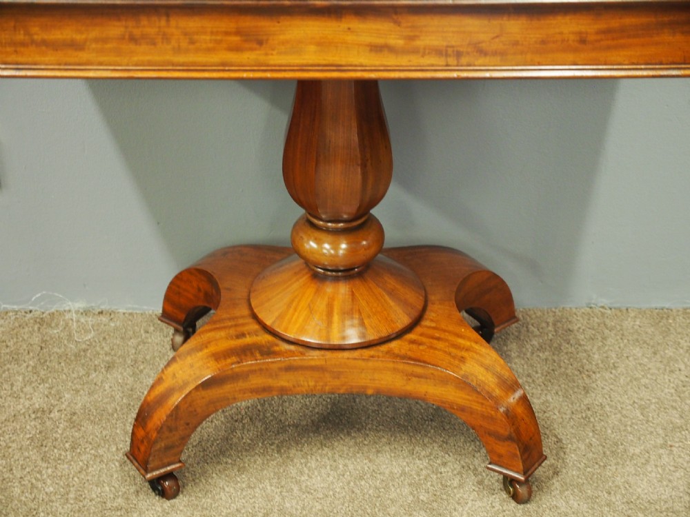 A 19th-century William IV mahogany fold-over table featuring a rounded rectangular top, a thick turned central pedestal, a concave quadform base, and brass castors. View IV