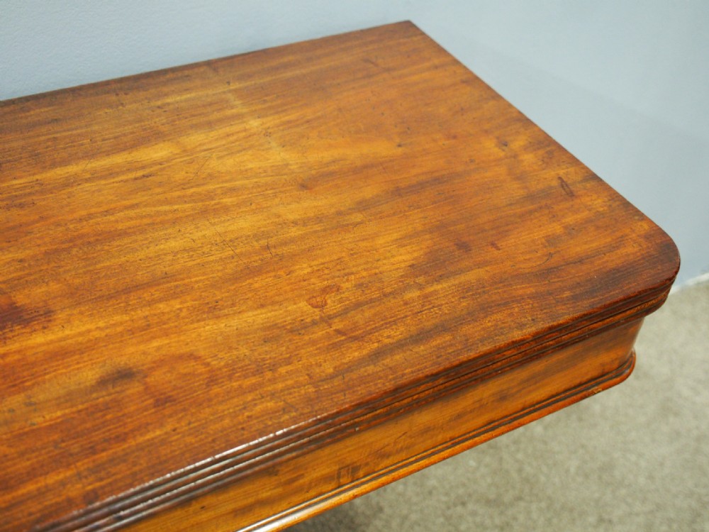 A 19th-century William IV mahogany fold-over table featuring a rounded rectangular top, a thick turned central pedestal, a concave quadform base, and brass castors. View VI
