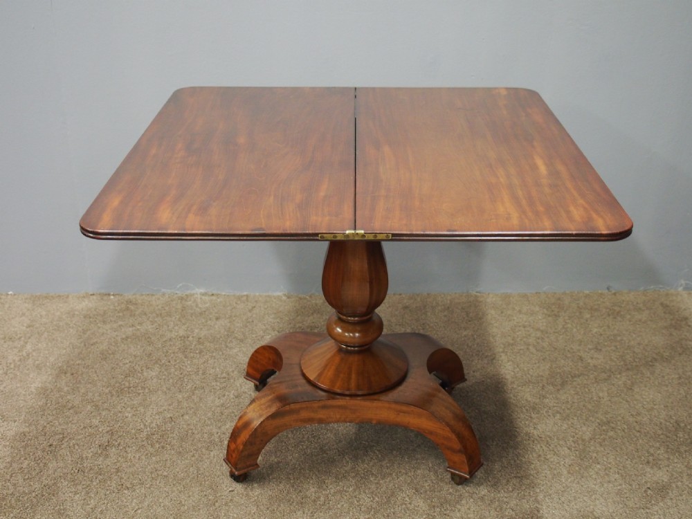 A 19th-century William IV mahogany fold-over table featuring a rounded rectangular top, a thick turned central pedestal, a concave quadform base, and brass castors. View VII