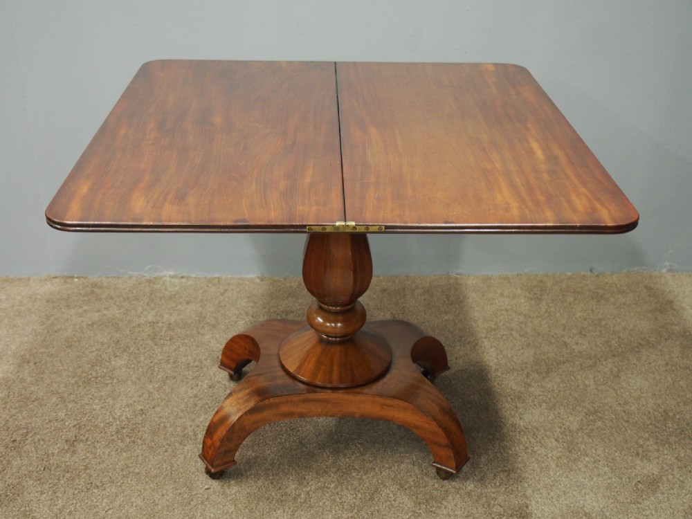 A 19th-century William IV mahogany fold-over table featuring a rounded rectangular top, a thick turned central pedestal, a concave quadform base, and brass castors. View VIII