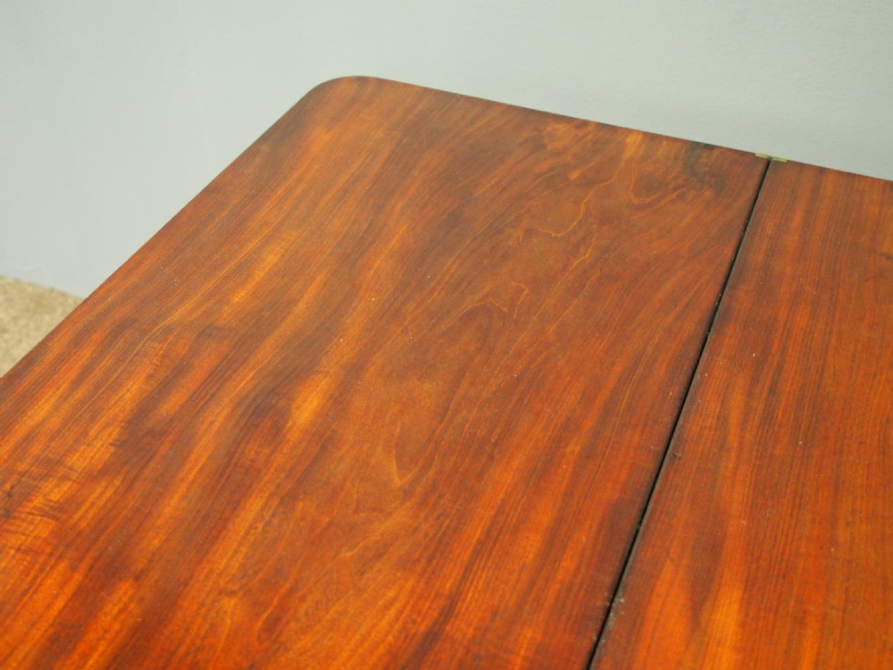 A 19th-century William IV mahogany fold-over table featuring a rounded rectangular top, a thick turned central pedestal, a concave quadform base, and brass castors. View X