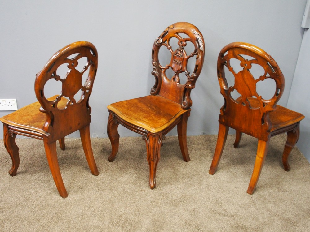 Set of three Victorian mahogany hall chairs featuring openwork carved backs inset with central heraldic crests and shaped front legs. View II