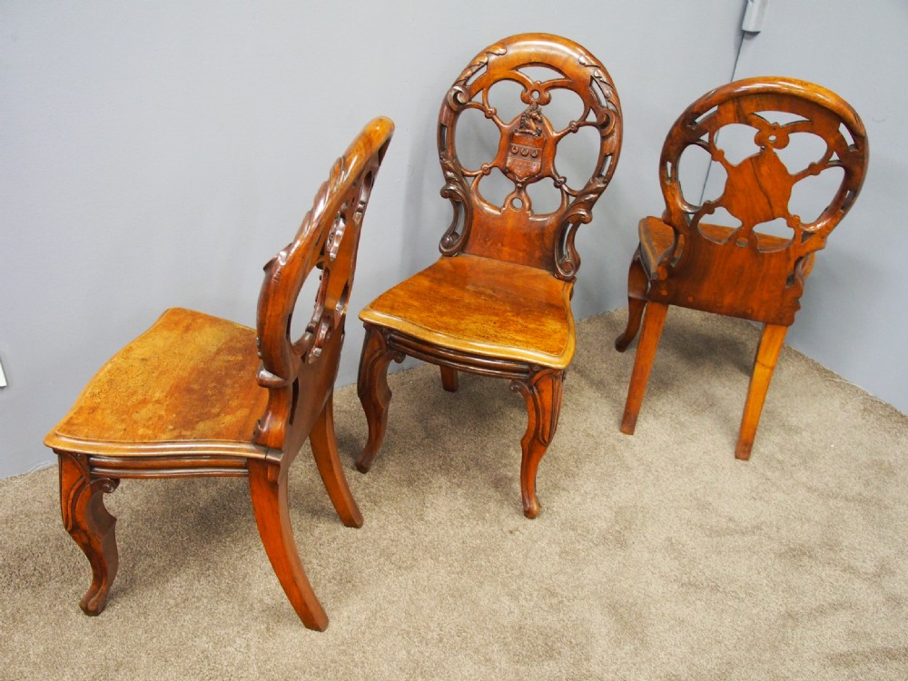 Set of three Victorian mahogany hall chairs featuring openwork carved backs inset with central heraldic crests and shaped front legs. View III