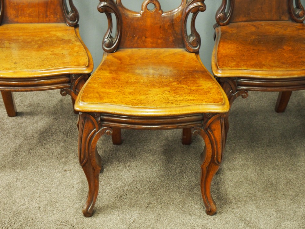 Set of three Victorian mahogany hall chairs featuring openwork carved backs inset with central heraldic crests and shaped front legs. View V