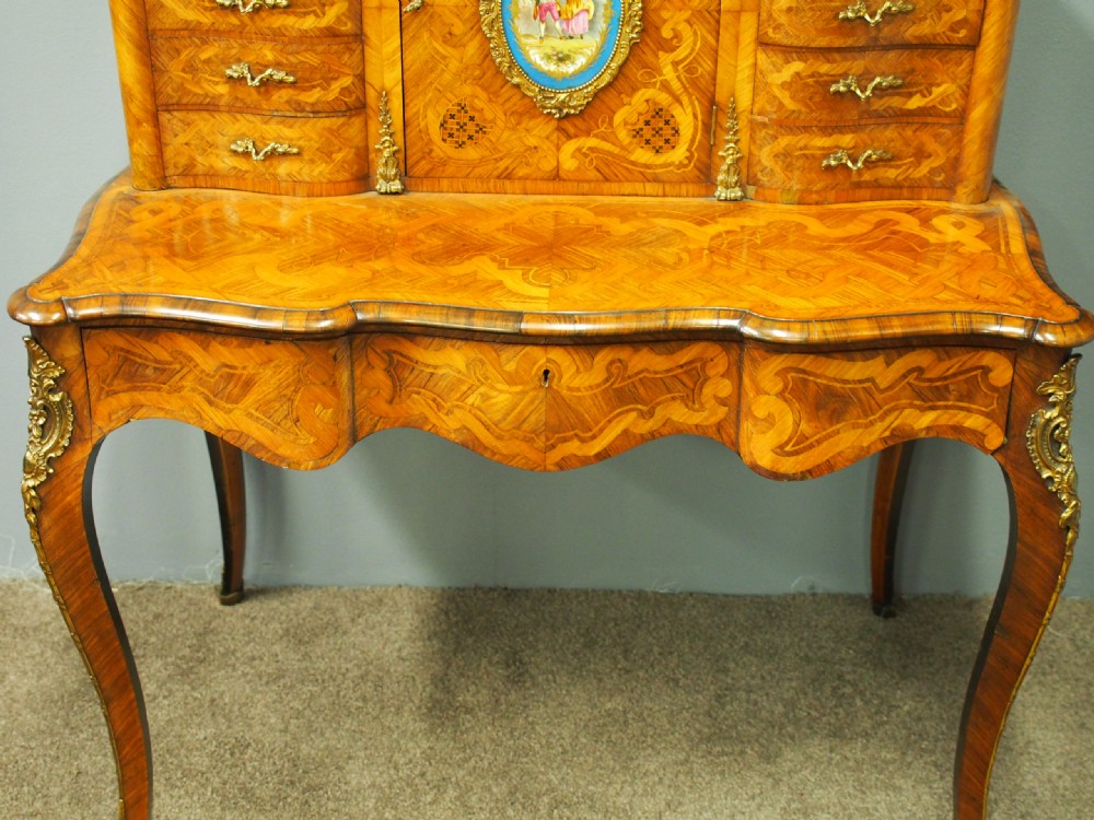 A French Rococo Revival ladies writing desk featuring intricate wood marquetry, gilt-bronze mounts, cabriole legs, and a central cabinet door set with a hand-painted porcelain plaque. View XI