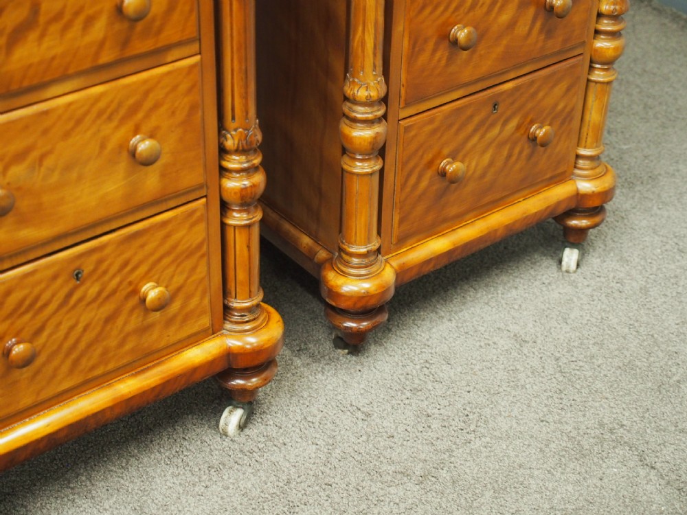 A pair of Victorian satin birch pedestal chests featuring four stacked drawers, turned corner columns, wooden knob handles, and castors. View V
