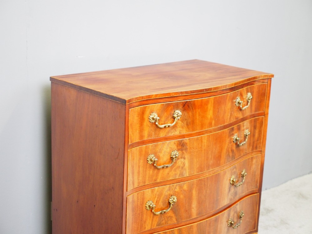 A Hepplewhite style mahogany chest of drawers featuring a serpentine front, four graduated drawers with cast brass handles, boxwood string inlay, and splayed bracket feet. View II