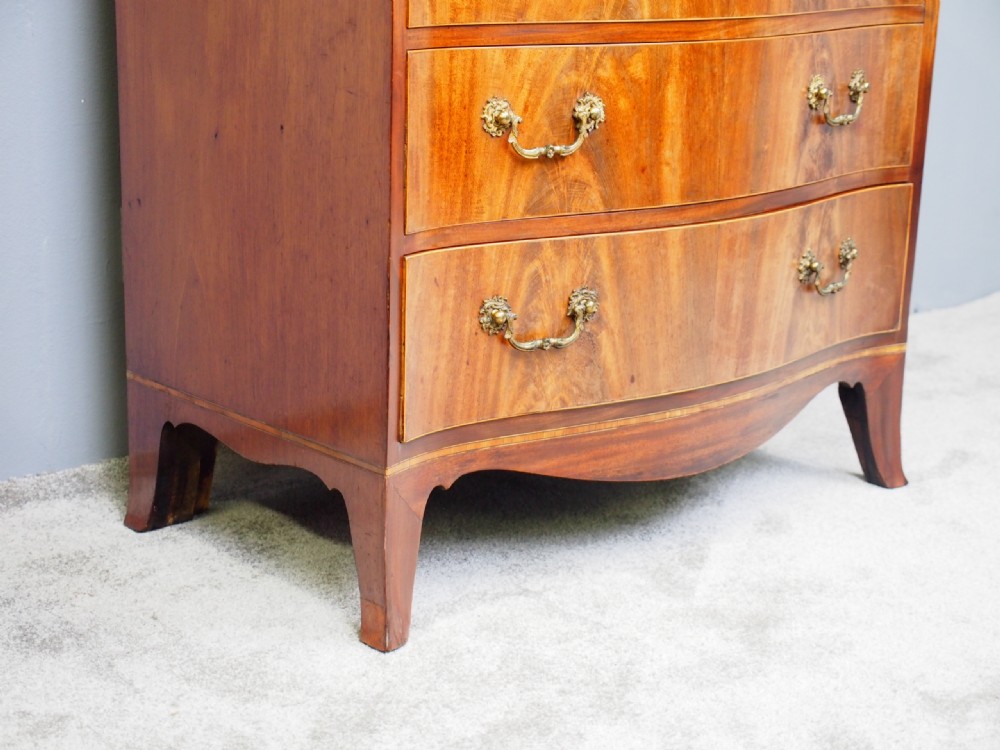 A Hepplewhite style mahogany chest of drawers featuring a serpentine front, four graduated drawers with cast brass handles, boxwood string inlay, and splayed bracket feet. View IV