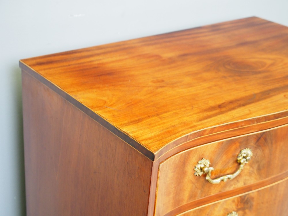 A Hepplewhite style mahogany chest of drawers featuring a serpentine front, four graduated drawers with cast brass handles, boxwood string inlay, and splayed bracket feet. View VI