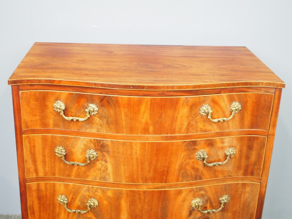 A Hepplewhite style mahogany chest of drawers featuring a serpentine front, four graduated drawers with cast brass handles, boxwood string inlay, and splayed bracket feet. View VII