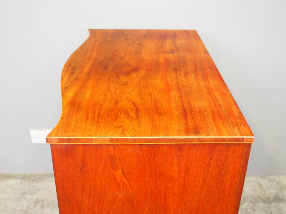 A Hepplewhite style mahogany chest of drawers featuring a serpentine front, four graduated drawers with cast brass handles, boxwood string inlay, and splayed bracket feet. View X