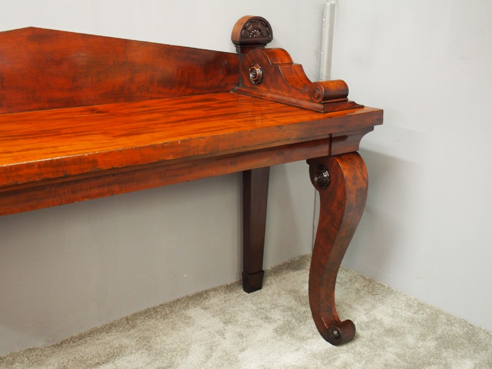A Scottish Regency mahogany serving table featuring a raised shaped gallery back with carved round scroll details and curved front legs. View VIII