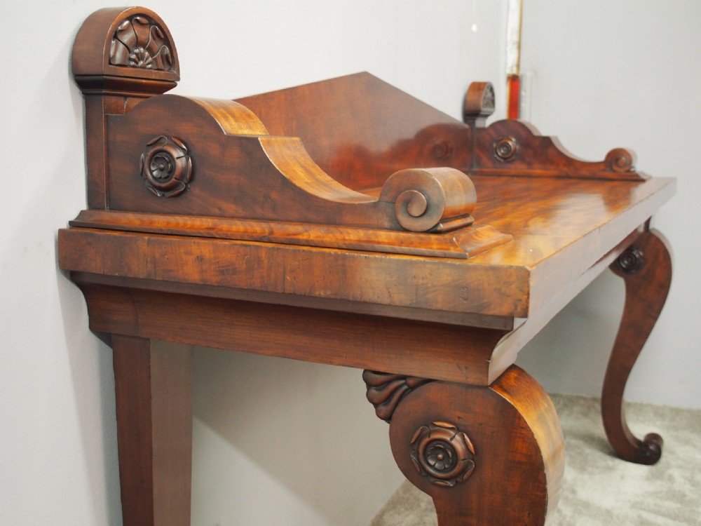 A Scottish Regency mahogany serving table featuring a raised shaped gallery back with carved round scroll details and curved front legs. View XI