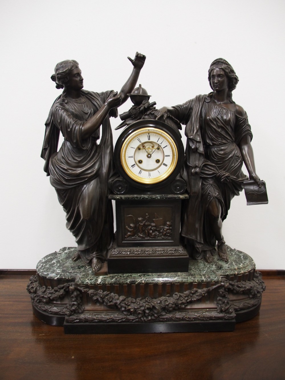 A three-piece French antique clock garniture featuring a central mantel clock flanked by classical female figures and two standalone bronze male sculptures on dark marble bases. View II