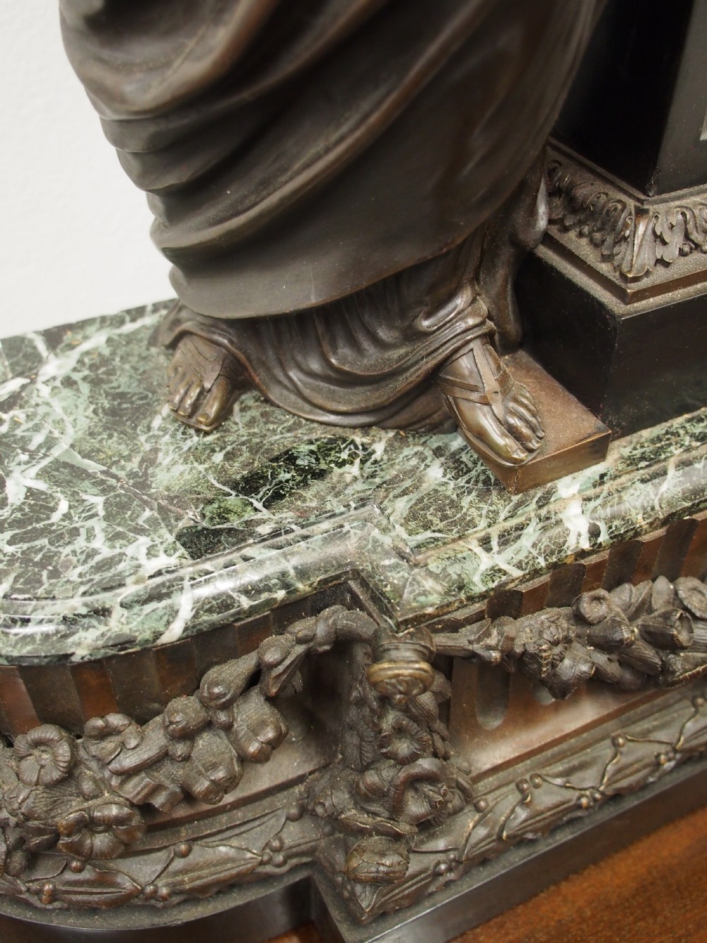 A three-piece French antique clock garniture featuring a central mantel clock flanked by classical female figures and two standalone bronze male sculptures on dark marble bases. View VI