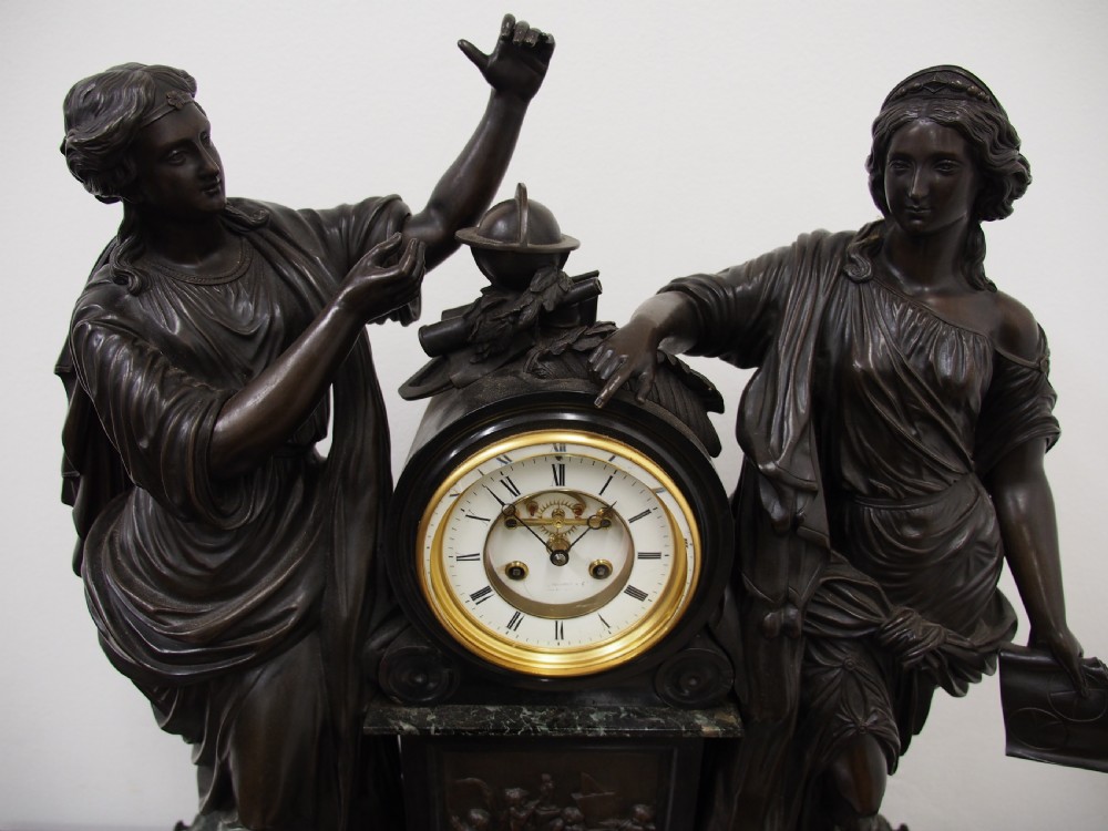 A three-piece French antique clock garniture featuring a central mantel clock flanked by classical female figures and two standalone bronze male sculptures on dark marble bases. View VII