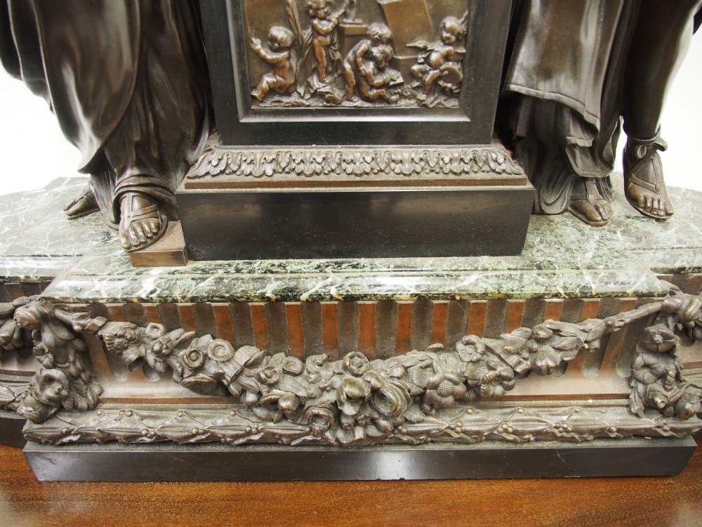 A three-piece French antique clock garniture featuring a central mantel clock flanked by classical female figures and two standalone bronze male sculptures on dark marble bases. View VIII
