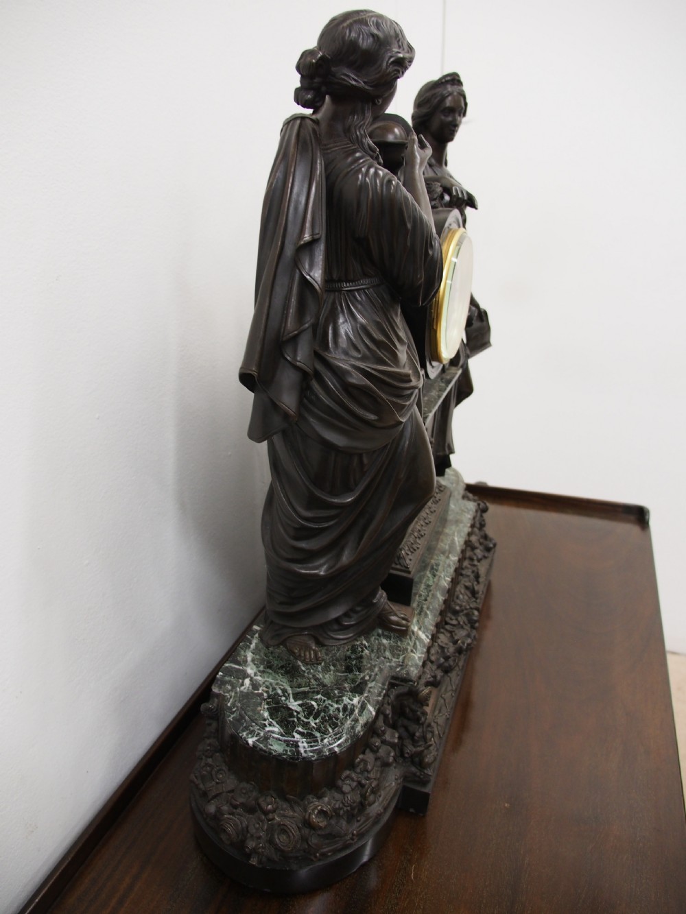 A three-piece French antique clock garniture featuring a central mantel clock flanked by classical female figures and two standalone bronze male sculptures on dark marble bases. View IX