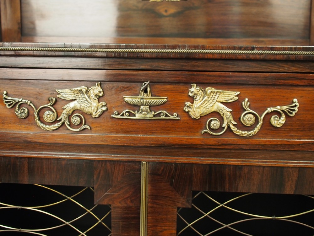 An antique Regency rosewood secretaire chiffonier featuring an upper tier shelf with S-scroll supports, brass mounts, and double doors with brass wire grilles. View VI