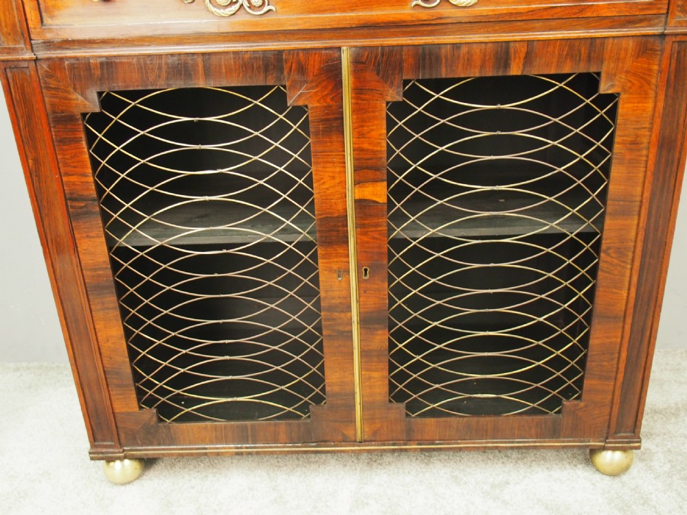 An antique Regency rosewood secretaire chiffonier featuring an upper tier shelf with S-scroll supports, brass mounts, and double doors with brass wire grilles. View VII