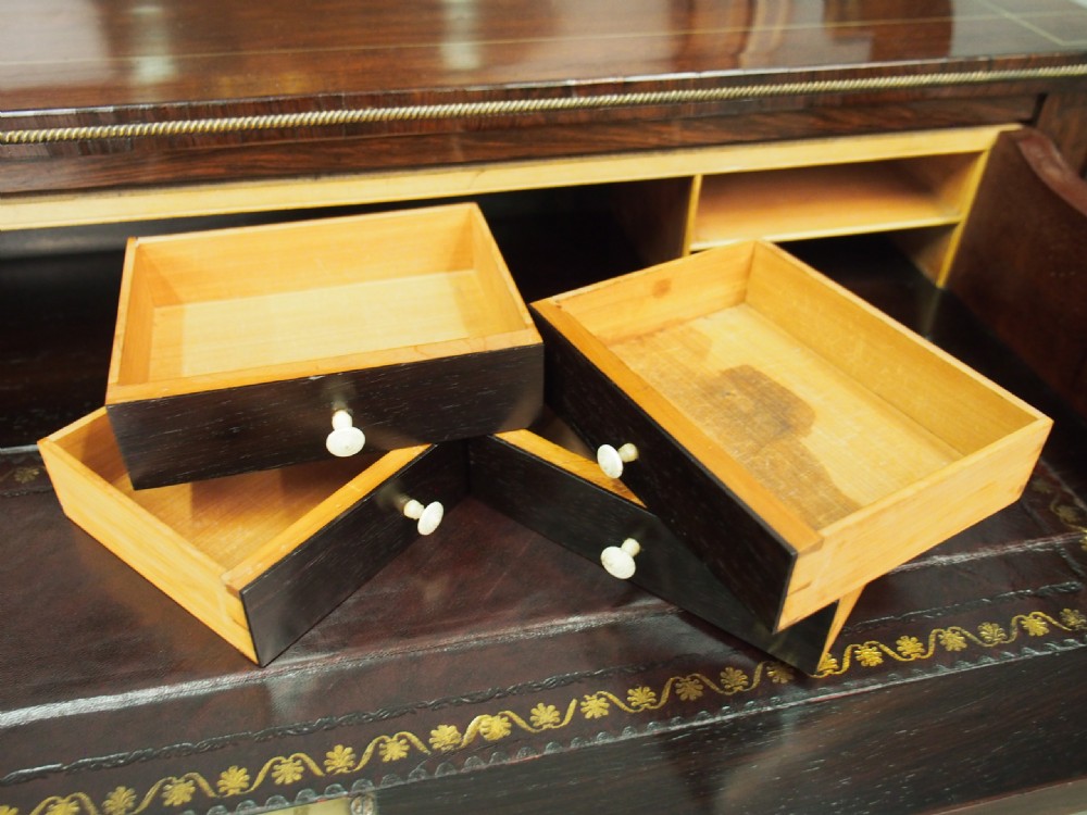 An antique Regency rosewood secretaire chiffonier featuring an upper tier shelf with S-scroll supports, brass mounts, and double doors with brass wire grilles. View X