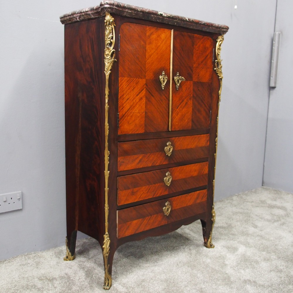 A Louis XV style kingwood cabinet featuring geometric parquetry veneering, a red-toned marble top, two upper cabinet doors, three lower drawers, and gilt-bronze ormolu mounts.