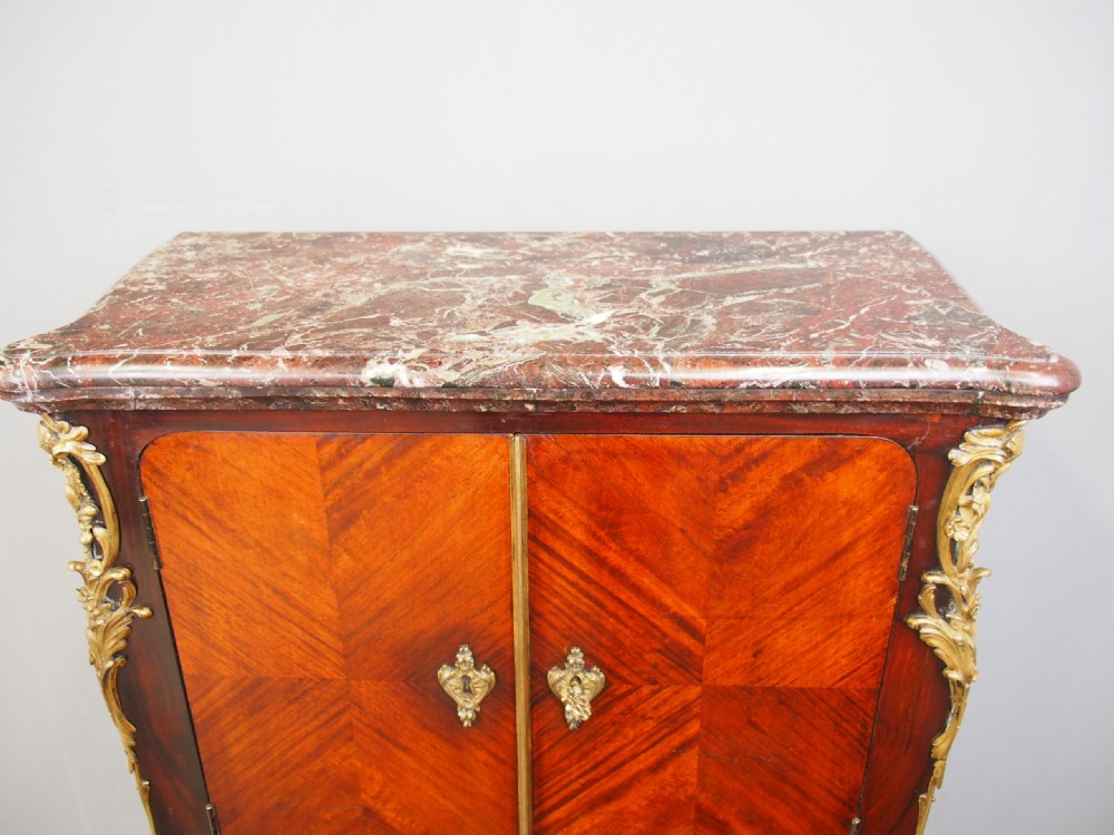 A Louis XV style kingwood cabinet featuring geometric parquetry veneering, a red-toned marble top, two upper cabinet doors, three lower drawers, and gilt-bronze ormolu mounts. View III